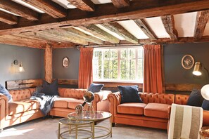 A cozy room with a wooden ceiling, a large window with curtains, a sofa set, and a round table with decorative items.