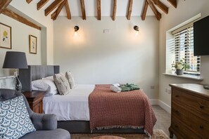 A bedroom with a bed, bedside table, lamp, and a window with blinds.