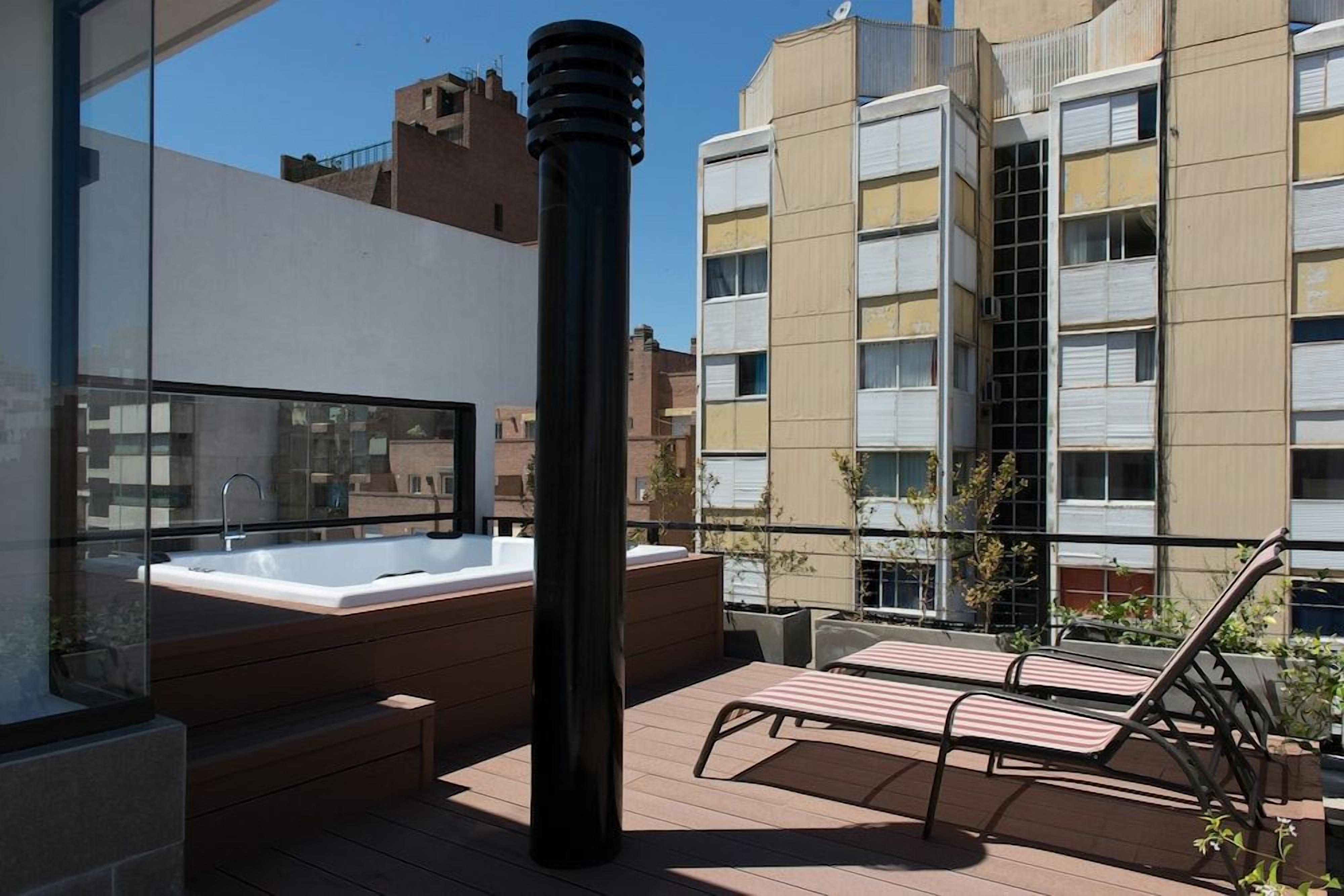 A rooftop terrace with a hot tub, lounge chairs, and a glass balustrade.