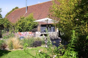 Ein Garten mit Außenbestuhlung, einer Holzkonstruktion und einem Backsteinhaus im Hintergrund.