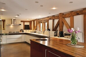 A modern kitchen with wooden beams, a central island with a sink, and a chalkboard sign. - The Manor Barn  -  a holiday let that sleeps 10 guests  in 5 bedrooms (Canterbury)