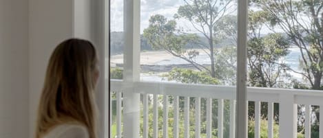 Una persona sentada junto a un ventanal con vistas a árboles y una playa.