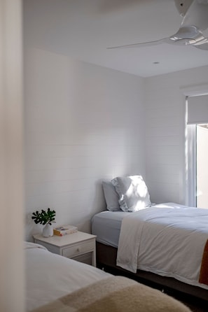 Un dormitorio con dos camas, una mesita de noche con una planta y una ventana.