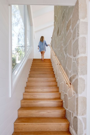 Una escalera de madera con paredes de piedra y ventanas amplias.