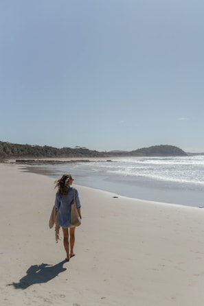 Una persona caminando sobre una playa arenosa con cielo despejado.