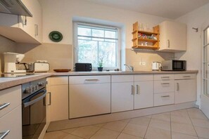 A modern kitchen with white cabinetry, a built-in oven, a microwave, and a window providing natural light. - Holiday home with 3 bedrooms (St.Peter-Ording)