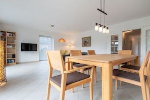 A modern dining area with a wooden table and chairs, a flat-screen TV, and a bookshelf. - Holiday home with 3 bedrooms (St.Peter-Ording)
