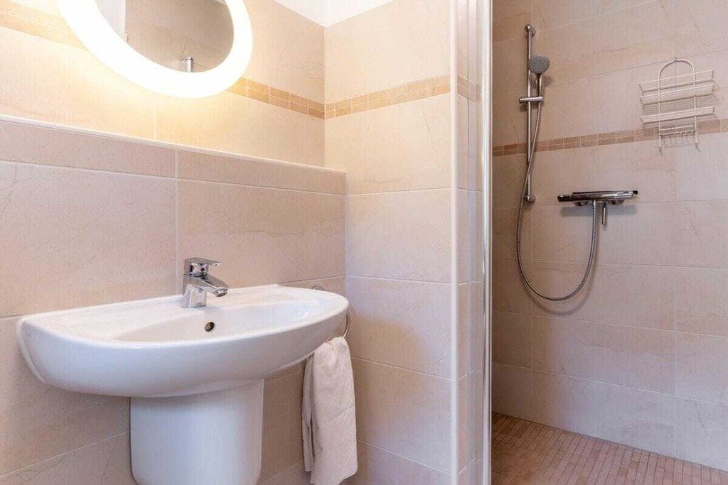 A bathroom with a white sink, a handheld showerhead, and a towel rack.