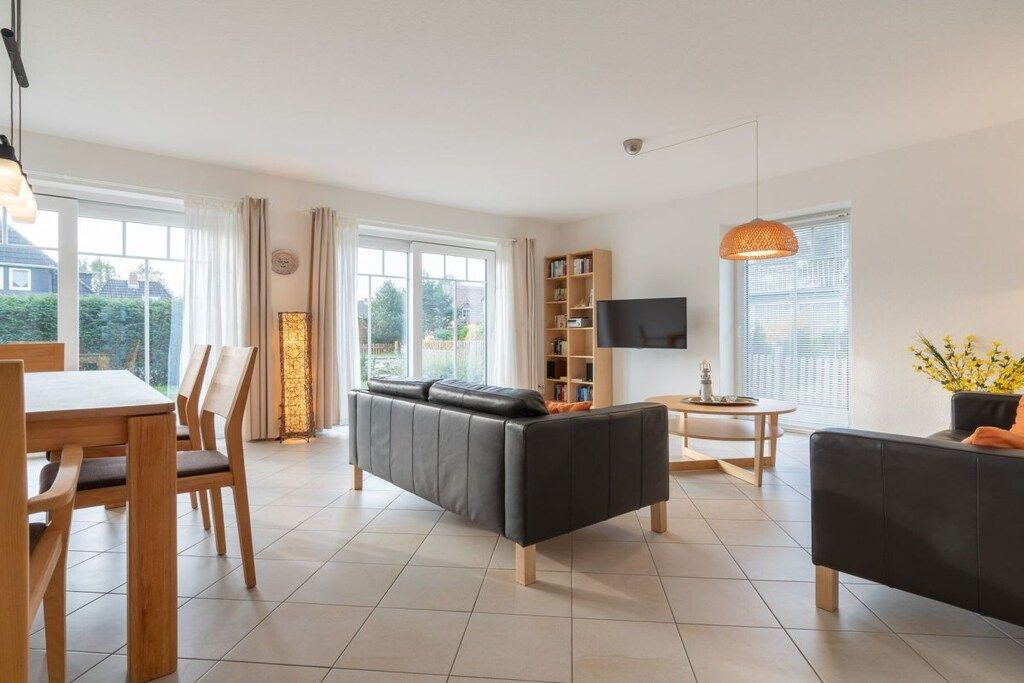 A modern living room with a sofa, a dining table with chairs, a TV, and a bookshelf.
