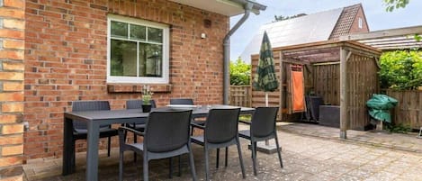 A brick house with a patio table and chairs, a wooden shed, and a covered outdoor area.
