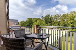 A balcony with wicker chairs and a glass table, overlooking a green landscape and a building with a tiled roof. - Holiday home with 3 bedrooms (St.Peter-Ording)