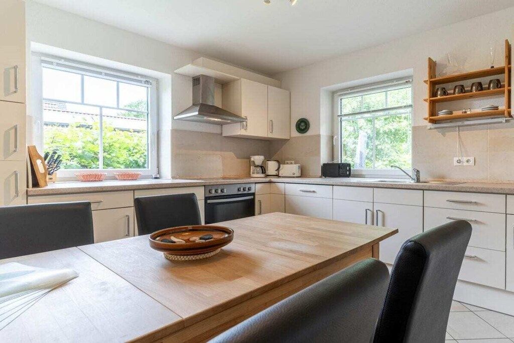 Une cuisine moderne avec des meubles blancs, une table à manger en bois et une cuisinière intégrée.
