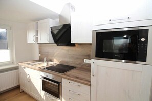 A modern kitchen with white cabinetry, a built-in oven, a microwave, and a black range hood. - Utholm 8 - Home port (St. Peter-Ording)