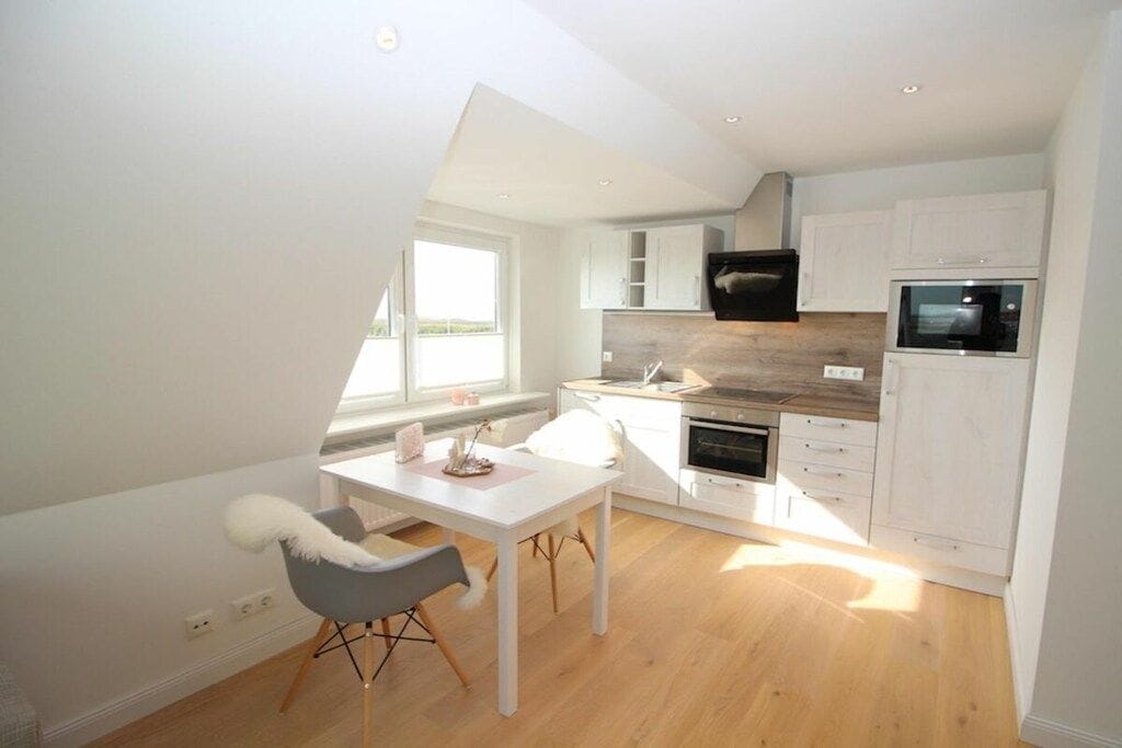 Une cuisine moderne avec des meubles blancs, un four à micro-ondes et un coin repas comprenant une table et des chaises.