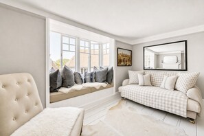 A room with a large window, a cushioned bench, a sofa, and a framed picture on the wall.