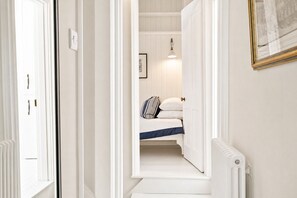 A narrow hallway with a bed at the end, a radiator, and a framed picture on the wall.