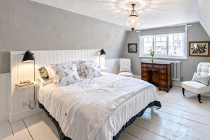 Ein Schlafzimmer mit einem großen Bett, Nachttischlampen, einem Schminktisch, einem Sessel und einem Fenster mit Blick.
