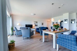 Ein modernes Wohnzimmer mit Essbereich, ausgestattet mit Fernseher, Sitzgelegenheiten und einer Küchenzeile mit gedecktem Tisch.