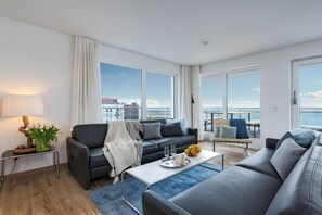A modern living room with a sofa, coffee table, and a view of the sea. - Holiday apartment with 1 bedroom (Ostseeresort Olpenitz)