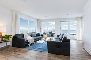A modern living room with a sofa, coffee table, and a view of the sea. - Holiday apartment with 1 bedroom (Ostseeresort Olpenitz)