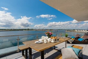 A dining table set with plates, cups, and a vase of flowers on a balcony overlooking a body of water. - Holiday apartment with 1 bedroom (Ostseeresort Olpenitz)