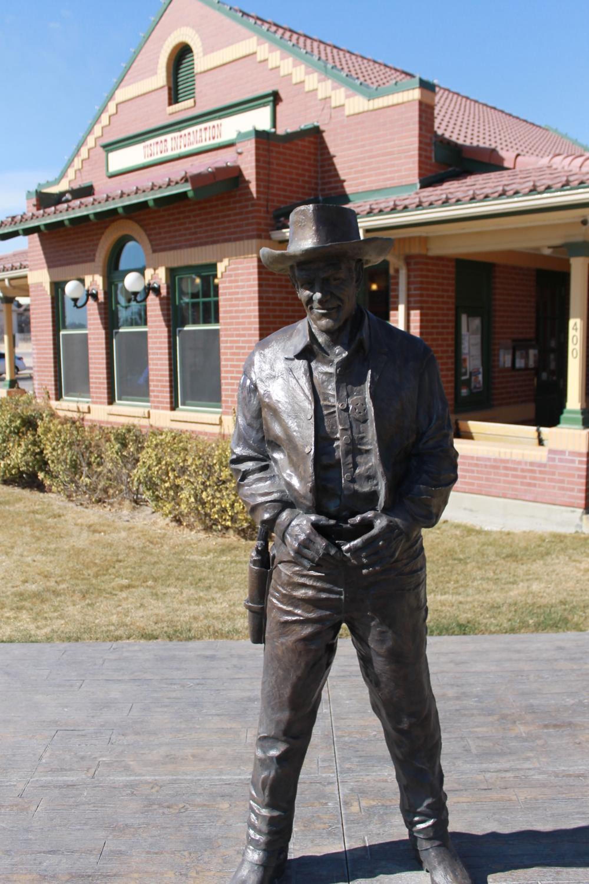 A statue of a man in a hat and vest standing in front of a building with a sign that reads 'Visitor Information.'