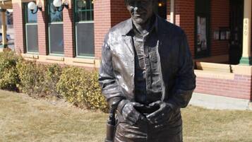 A statue of a man in a hat and vest standing in front of a building with a sign that reads 'Visitor Information.'