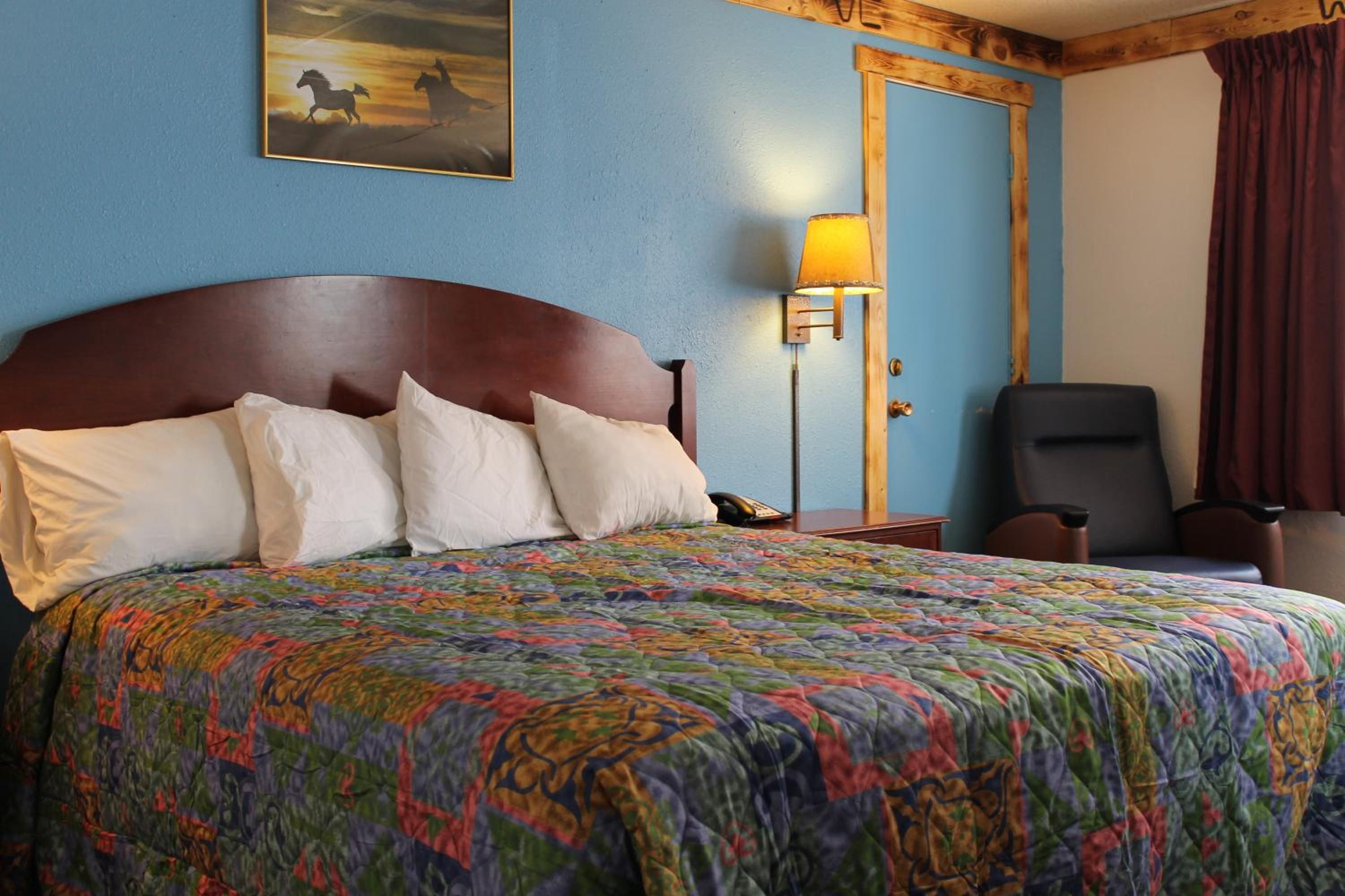 A hotel room with a large bed, a nightstand, a desk, a chair, a painting on the wall, and a door.