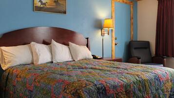A hotel room with a large bed, a nightstand, a desk, a chair, a painting on the wall, and a door.