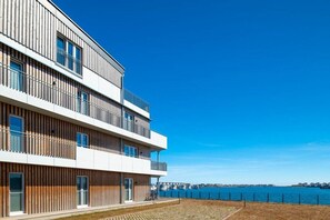 Ein mehrstöckiges Gebäude mit Balkonen, Blick auf das Wasser und einem klaren Himmel.
