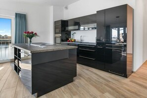 Une cuisine moderne dotée d’un îlot central, de meubles de rangement aux couleurs sombres et offrant une vue sur l’extérieur.