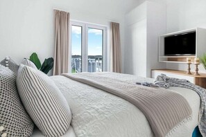 Ein modernes Hotelzimmer mit einem großen Bett, einem Flachbildfernseher und Blick auf die Stadt.