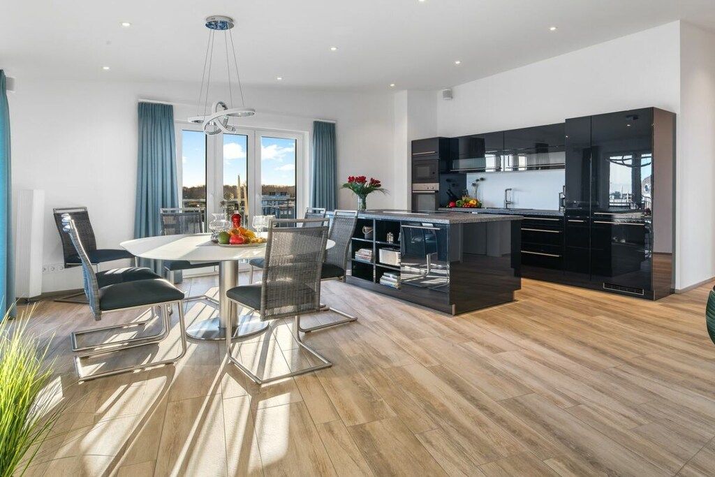 A modern kitchen with black cabinetry and a dining area with a glass table and chairs.