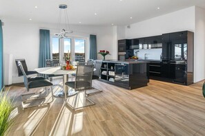 Une cuisine moderne avec des meubles de couleur noire et un coin repas comprenant une table et des chaises en verre.