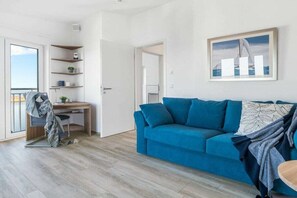 Ein modernes Wohnzimmer mit einem blauen Sofa, einem Holztisch und einem Balkon.