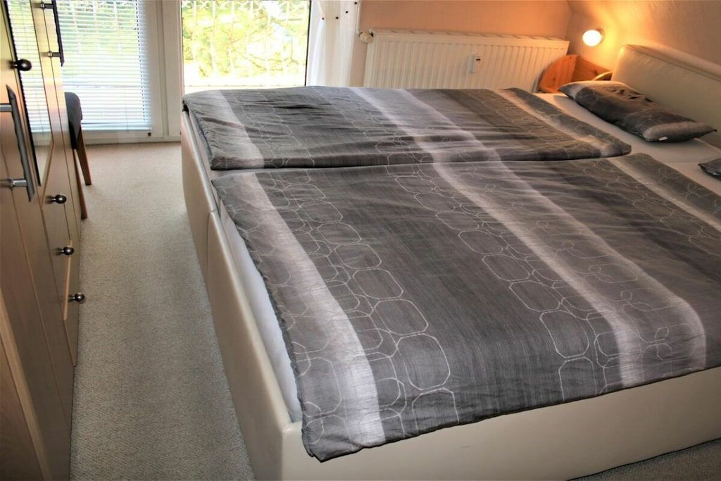 Une chambre à coucher avec un lit, une table de chevet, une lampe et une fenêtre avec des stores.