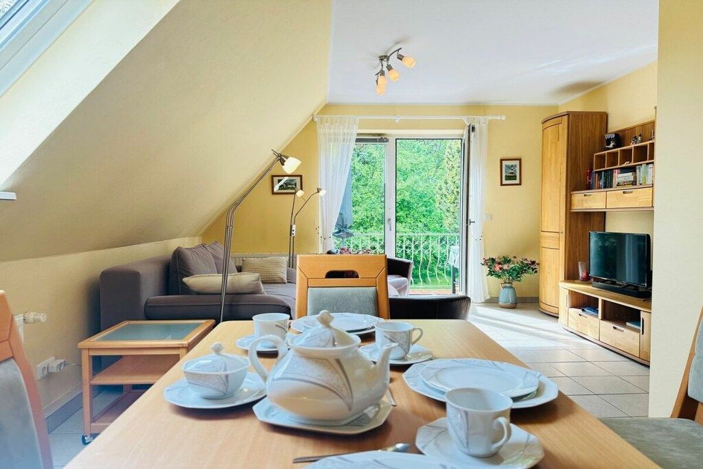 A dining area with a table set for tea, a sofa, a television, and a bookshelf.