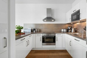 A modern kitchen with white cabinets, stainless steel appliances, and a wooden countertop. - Apartment in Olpenitz with swimming pool (Olpenitz)