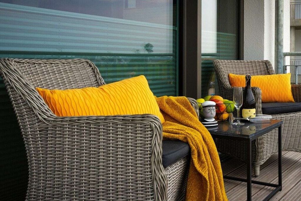 A wicker sofa with yellow cushions and a glass table with a bottle and fruit.