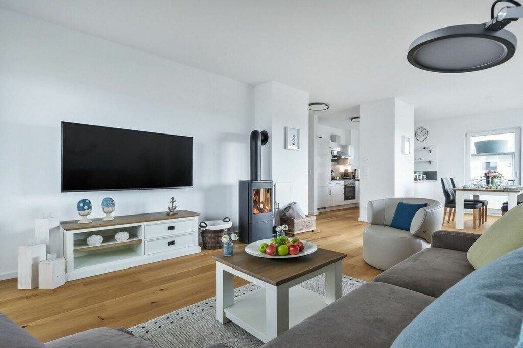 A modern living room with a flat-screen TV, a wood-burning stove, and a dining area with a table and chairs.