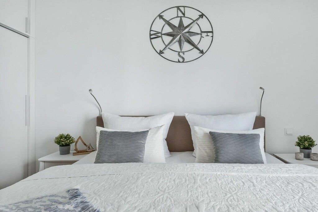 Une chambre à coucher avec un lit, des oreillers, une boussole fixée au mur et des tables de chevet ornées de plantes.