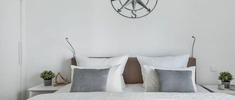 Une chambre à coucher avec un lit, des oreillers, une boussole fixée au mur et des tables de chevet ornées de plantes.