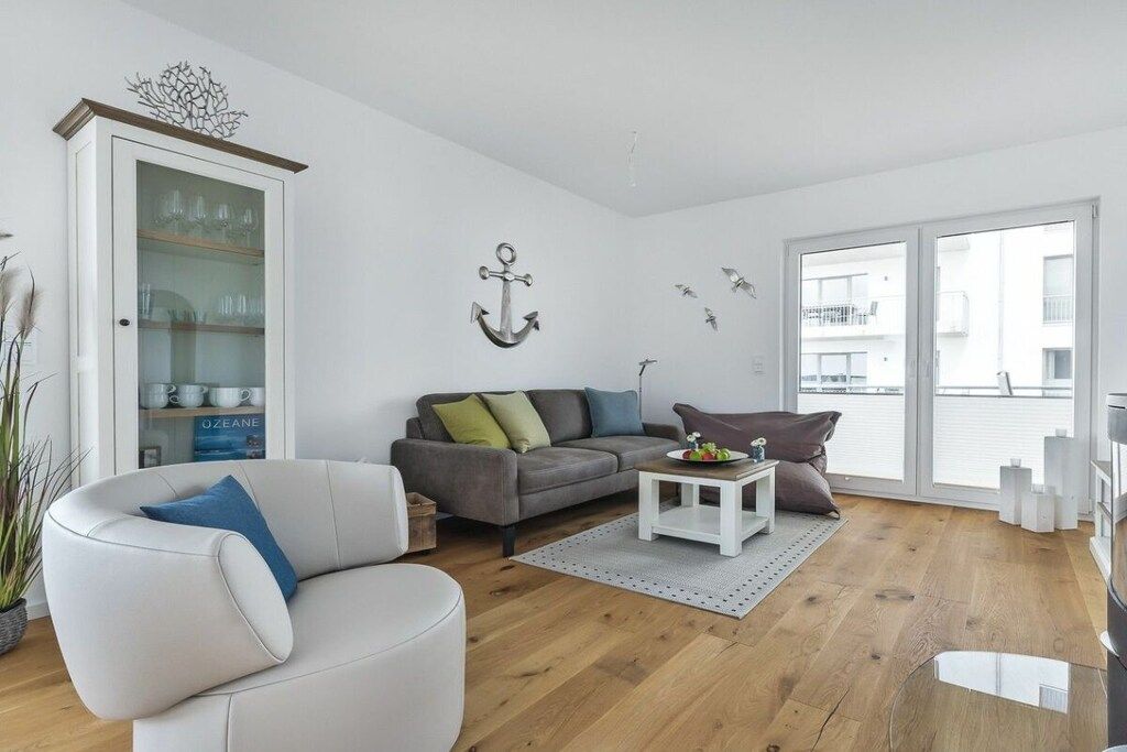 Een moderne woonkamer met een grijze bank, een witte fauteuil en een glazen kast.