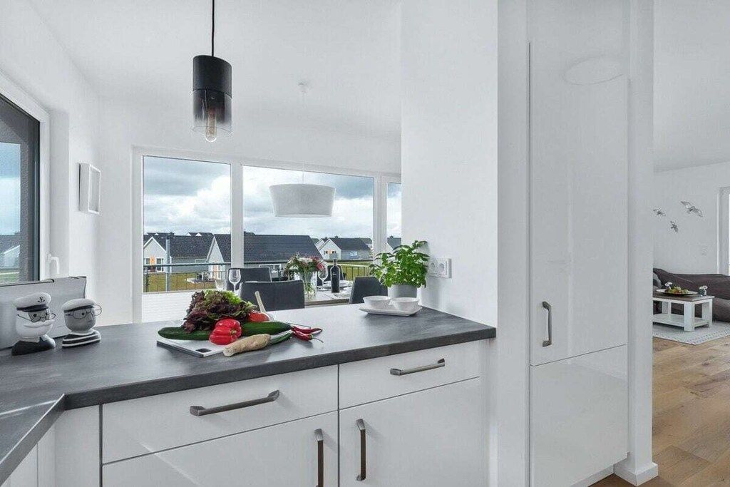A modern kitchen with a large window, a black pendant light, and a view of the neighborhood.