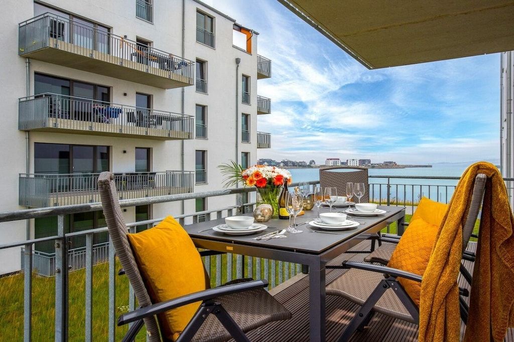 Un balcon avec une table dressée pour le dîner, donnant sur une étendue d’eau et sur des bâtiments.