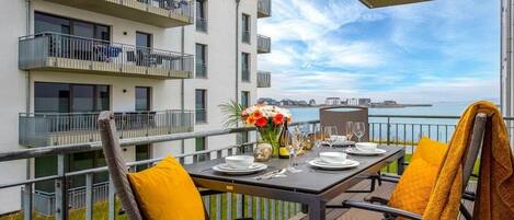A balcony with a table set for dining, overlooking a body of water and buildings.