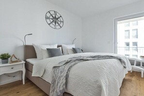 A bedroom with a bed, a nightstand, a wall-mounted compass decoration, and a window with a view of buildings. - Apartment in Kappeln with swimming pool (Kappeln)