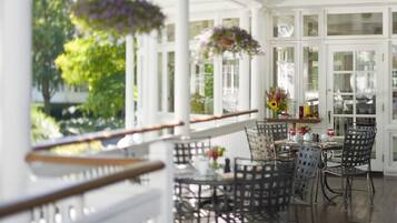 A covered outdoor dining area with metal chairs and a table, surrounded by white columns and glass doors.