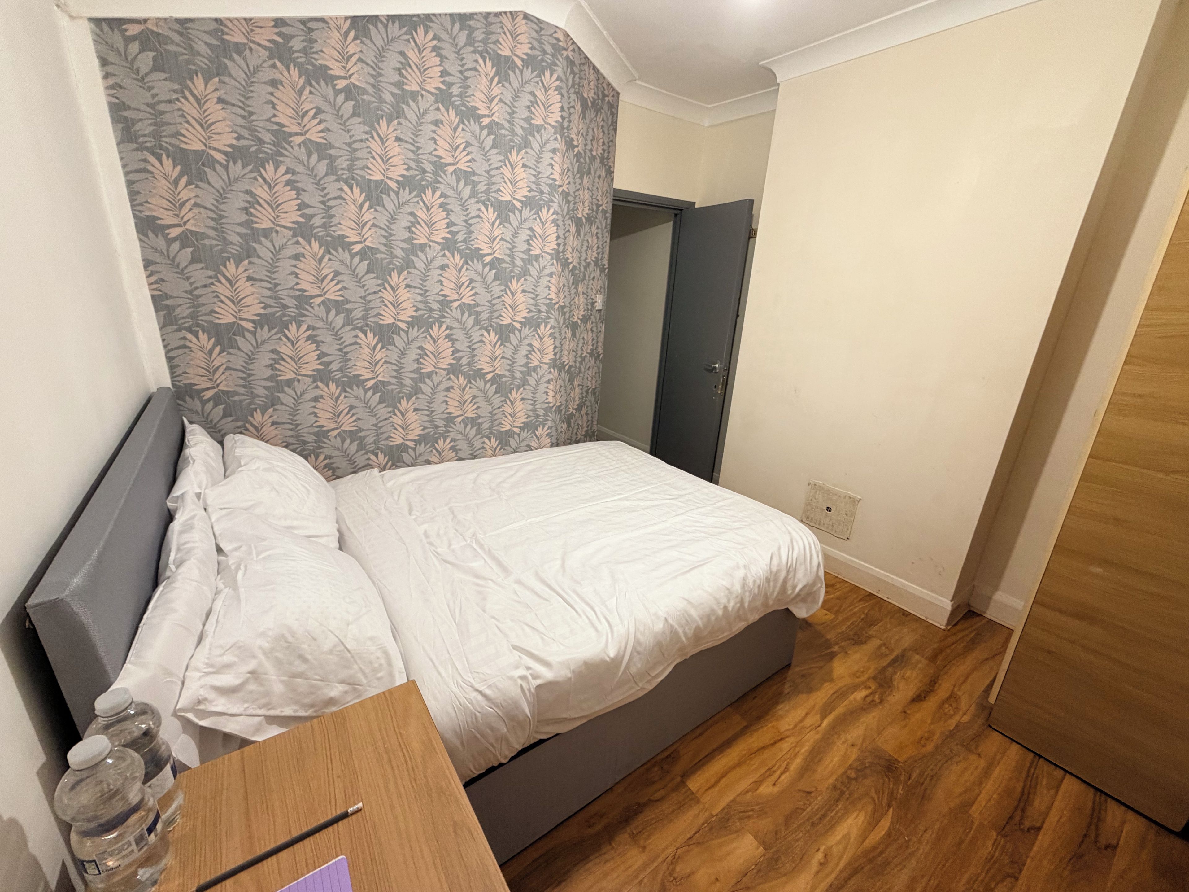 A bedroom with a bed, a desk with a chair, a mirror, and a wardrobe.