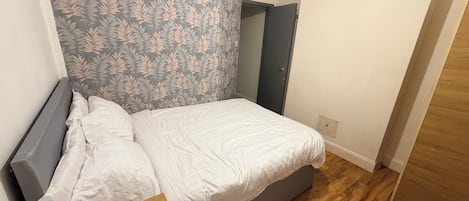 A bedroom with a bed, a desk with a chair, a mirror, and a wardrobe.